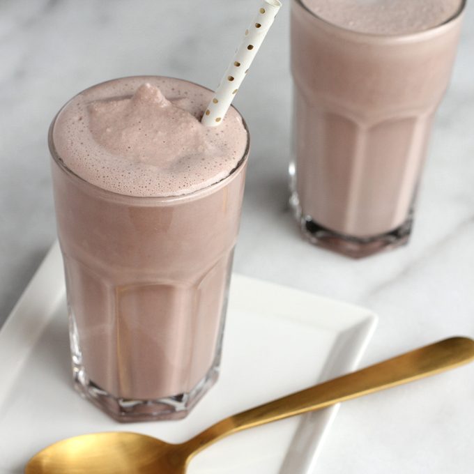 two copycat Wendy's chocolate frosty in clear cups with straws with a golden spoon on the side