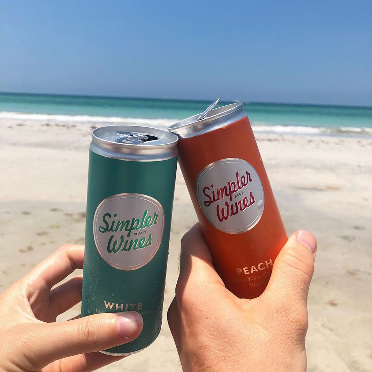 Simpler Wine cans cheersing on beach