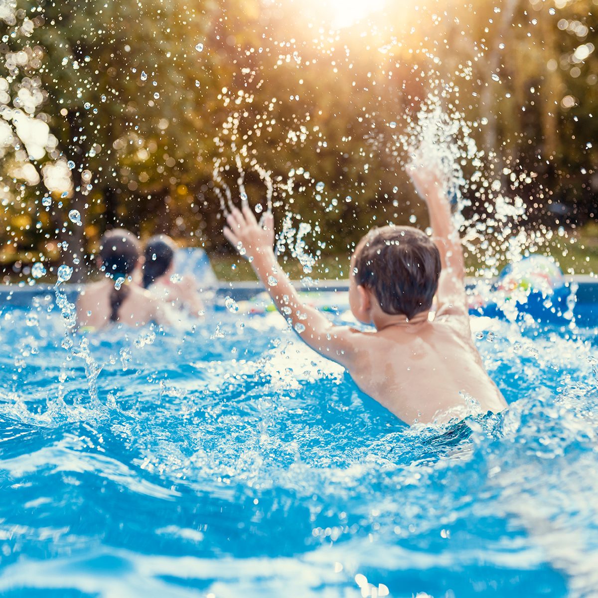Photo of Three Caucasian happy children playing and splashing on the swimming pool at the day time. Concept of friendly family.