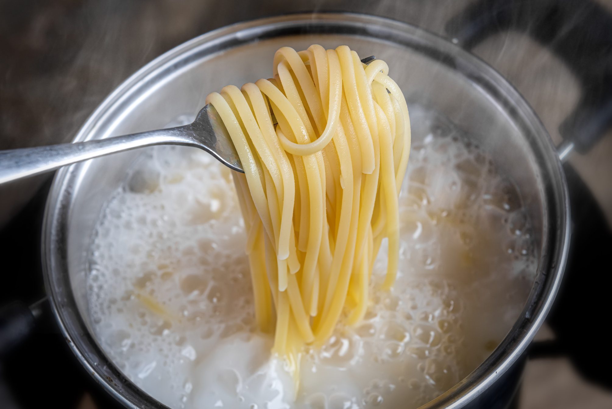 Yellow noodles or spaghetti cooking in boiling water pot.