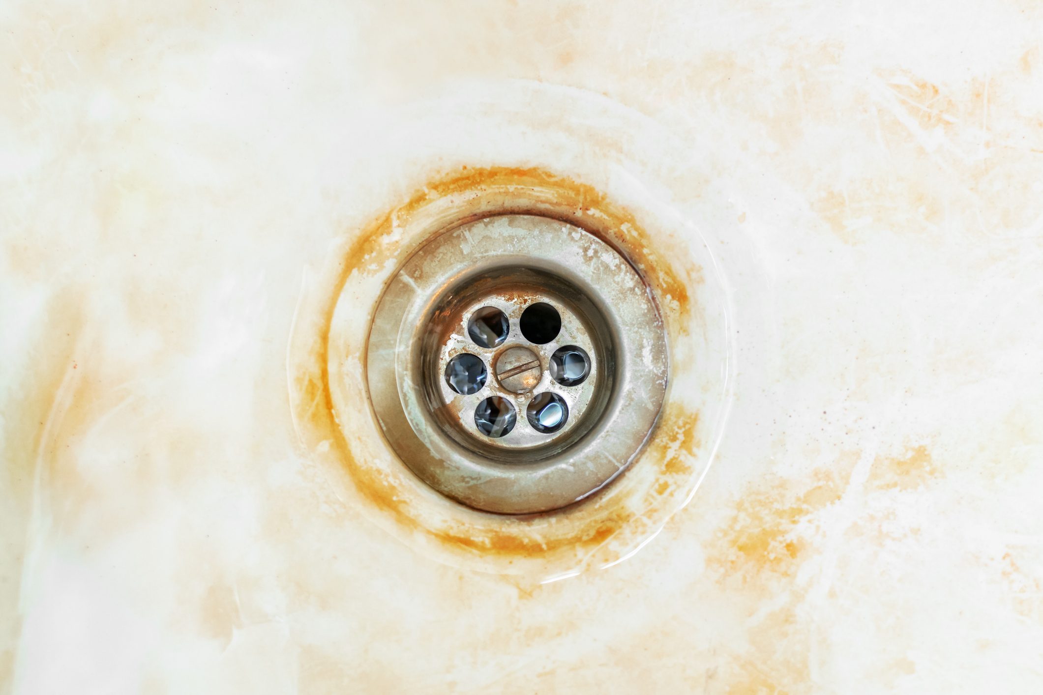 Old rusty bathtub with a metal drain hole. Dirty cracked unclean surface of the bath or sink with red rust stain, close-up. Corrosion, unsanitary.