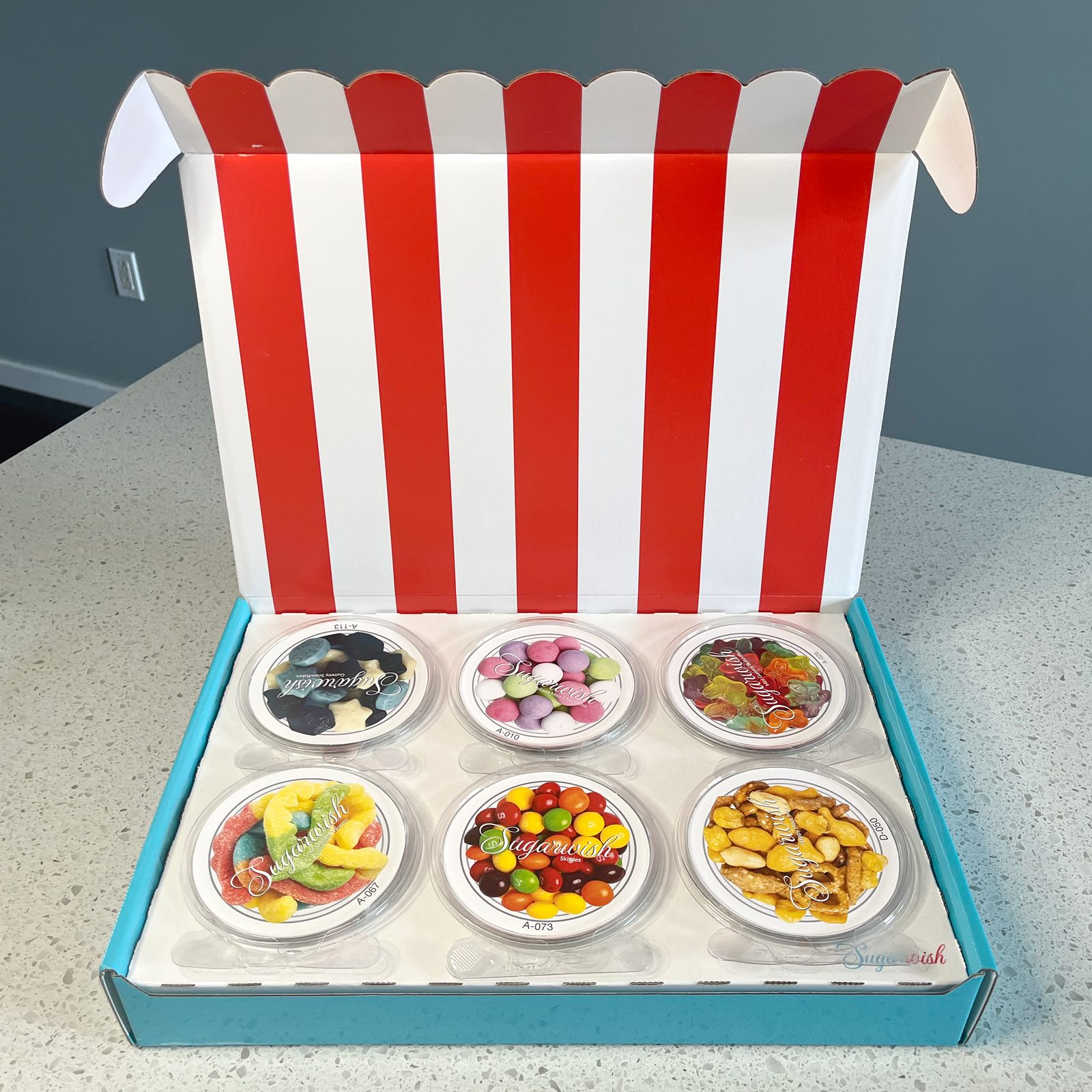 opening a sugar wish candy box to see sis small circular containers with lids labelled with pictures of the snacks and candies that are inside