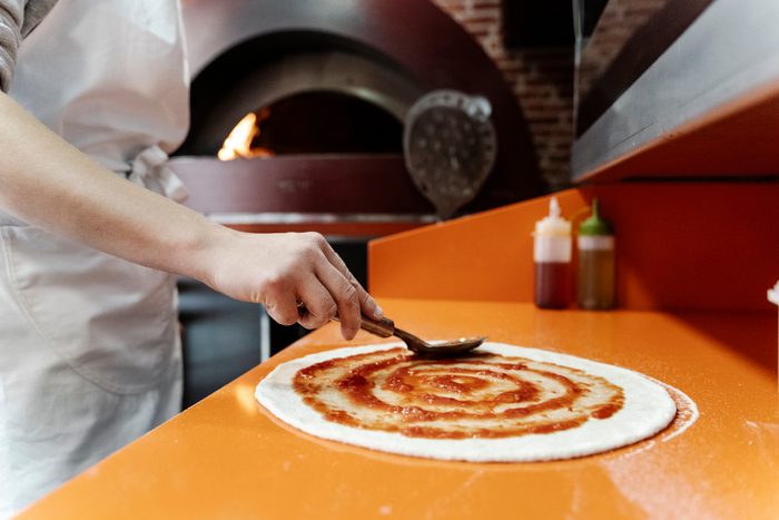 pizza maker topping the pizza with tomato sauce
