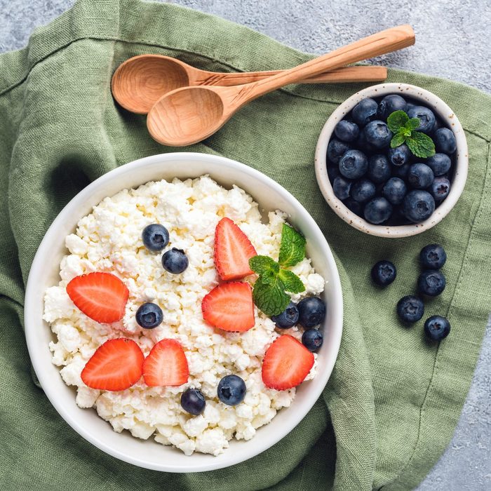cottage cheese in a bowl with strawberries and blueberries with two wooden spoons to the side and another smaller bowl filled with blueberries