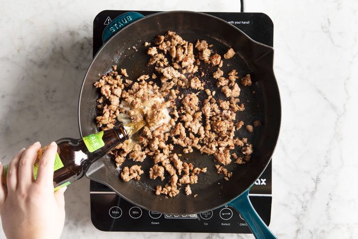 adding beer to browned beef in a cast iron skillet