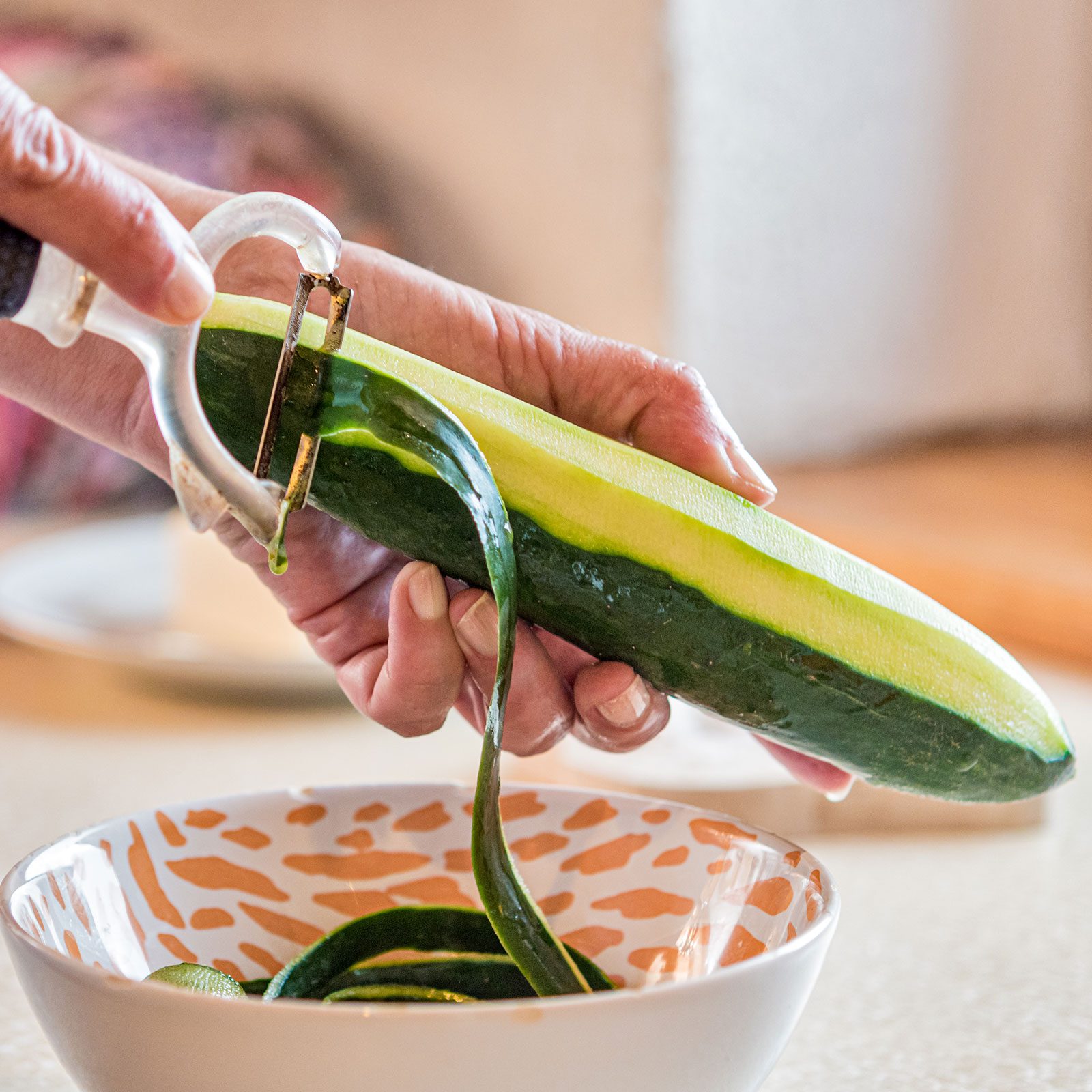 Woman Peeling Cucumber over a colorful bowl in a bright kitchen background