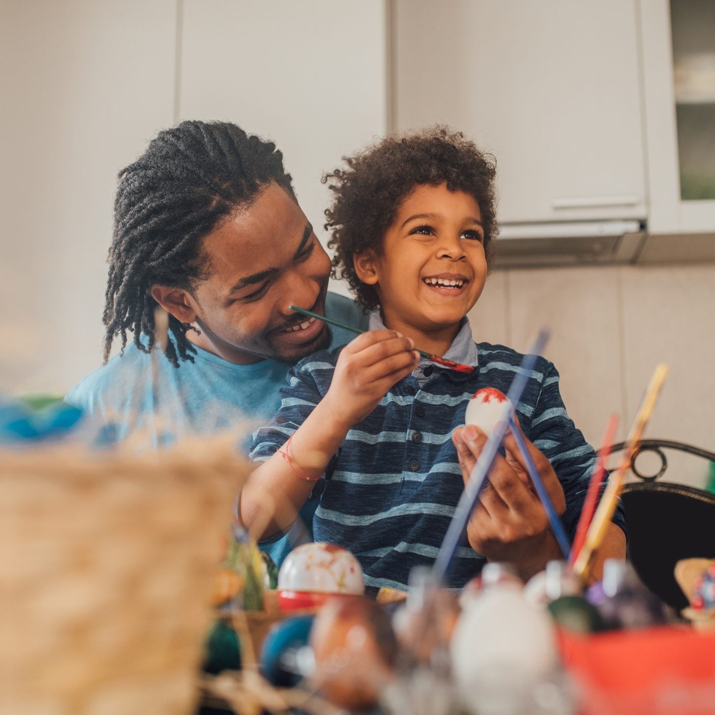 Smiling young boy coloring Easter eggs with his father at home