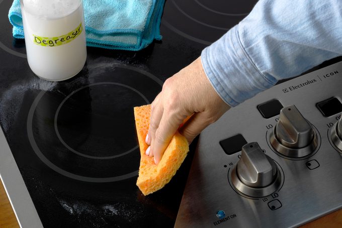 hand using a sponge and rubbing grime away on a stovetop