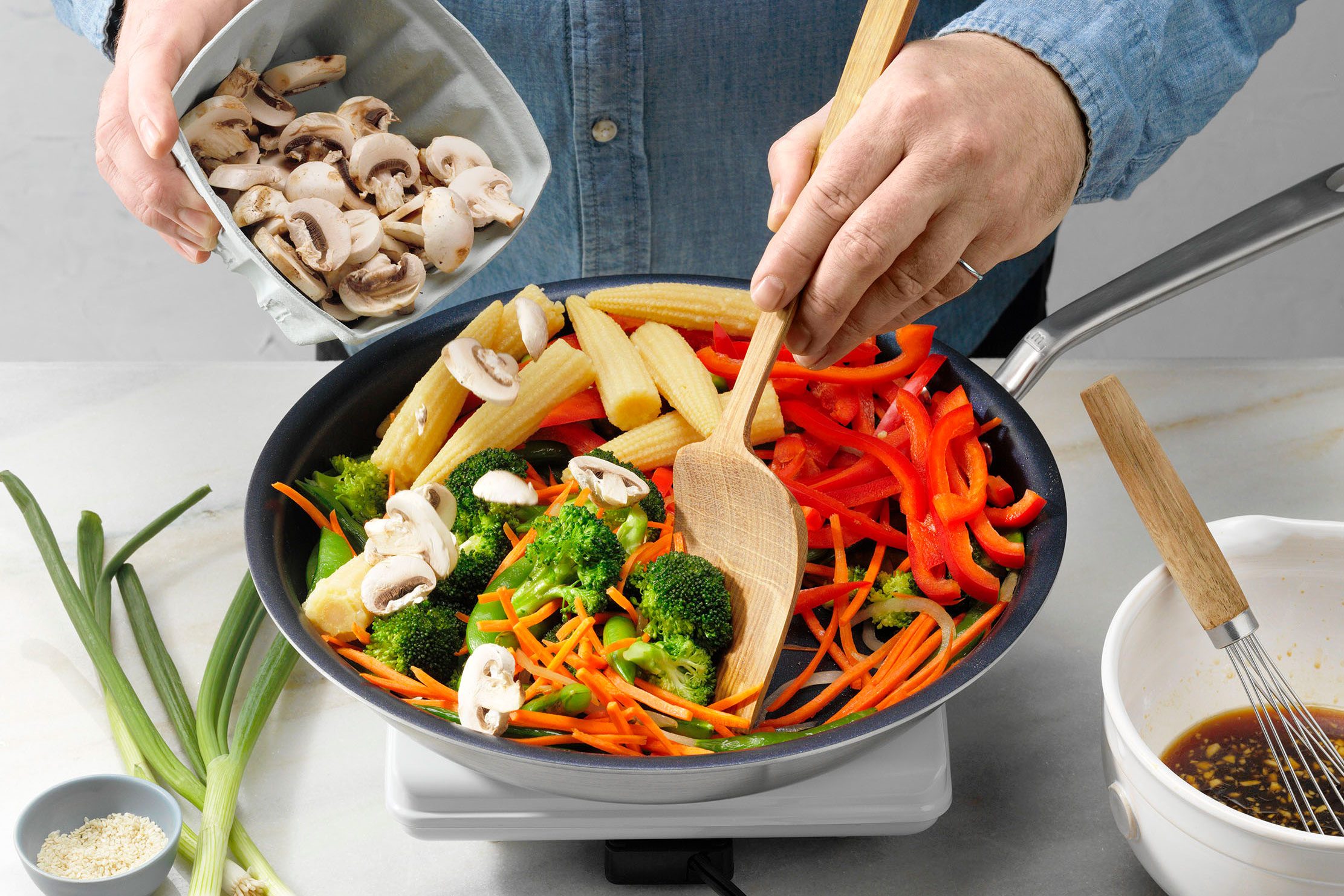 Vegan Stir-Fry showing broccoli peas carrots and onion already stir fried for five minutes; in process of adding mushrooms red pepper and corn