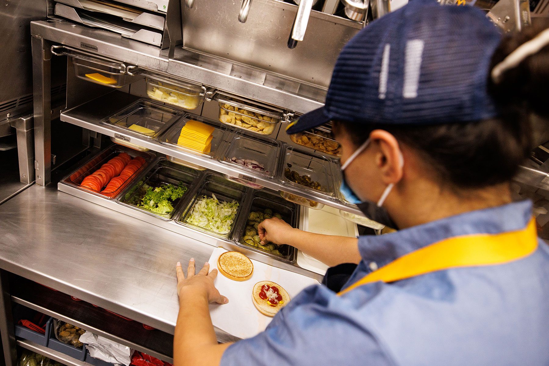 An employee takes a slice of cucumber from a compartment to prepare a cheeseburger at a branch of the McDonald's fast food chain