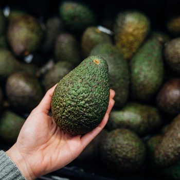 Woman choosing avocados in supermarket