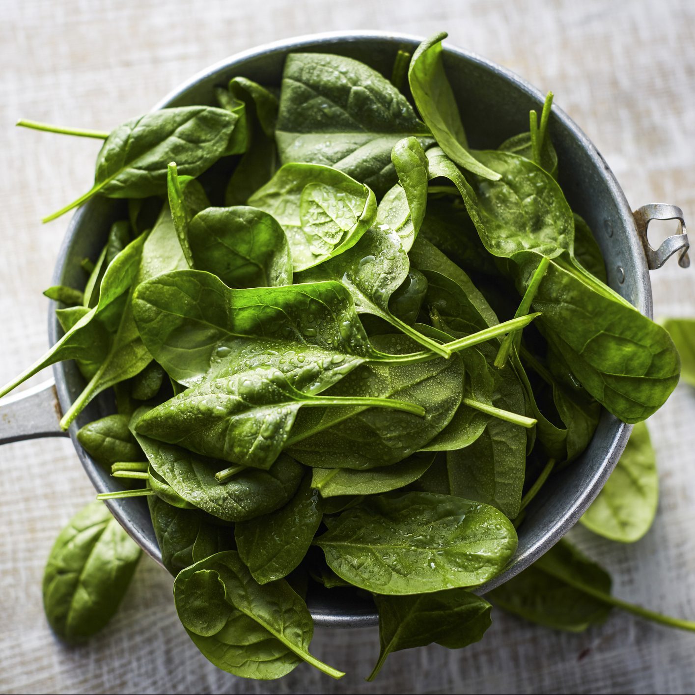 Fresh spinach leaves in colander on wood