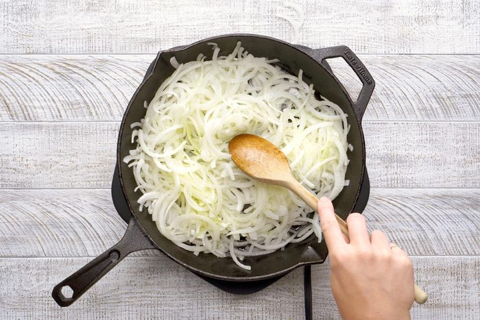 sautéing onions in a cast iron skillet wit ha wooden spoon