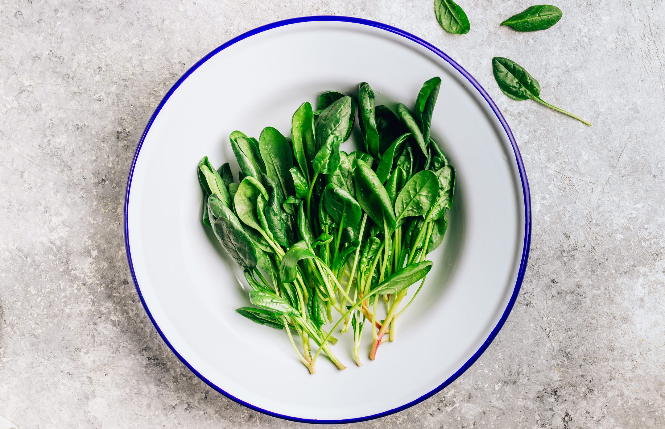 Fresh green baby spinach on plate on stone table