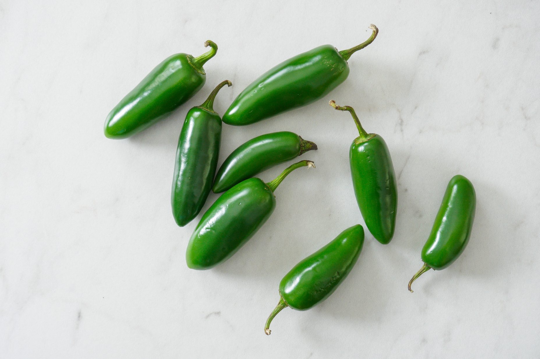Bright green jalapenos on a white marble cutting board with copy space