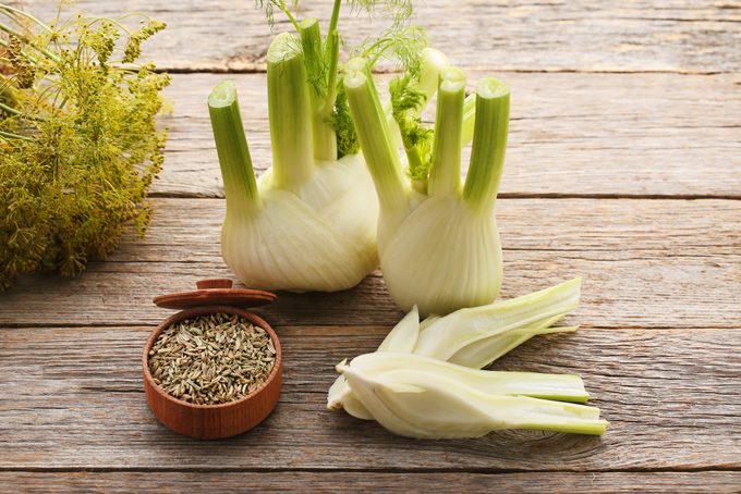 Ripe fennel bulbs and dry seeds in bowl on grey wooden table