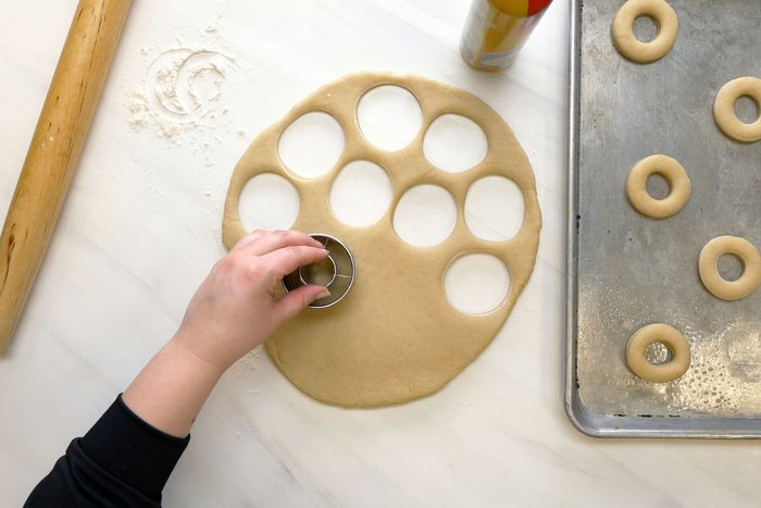 A person cutting the dough for doughnuts