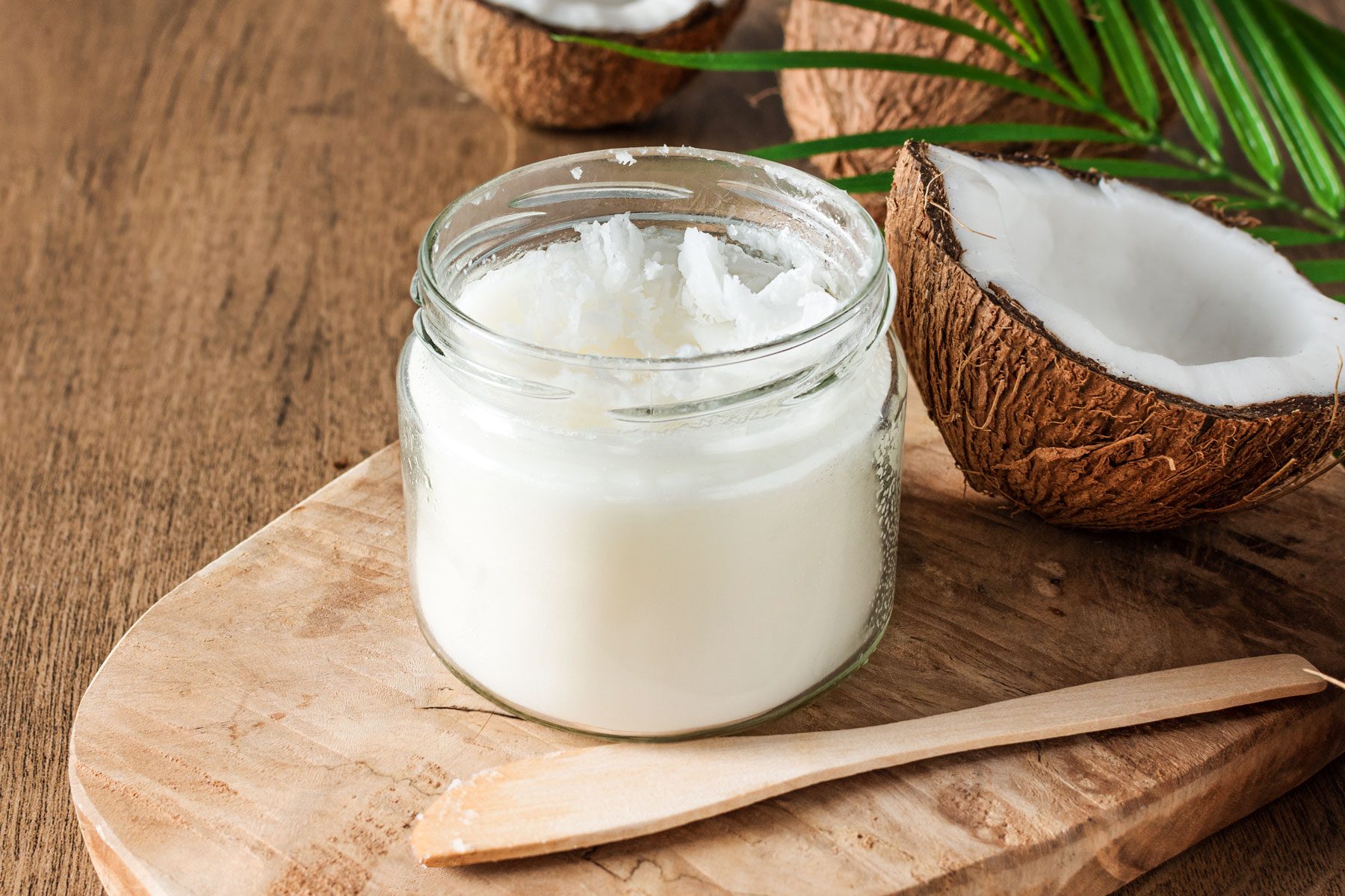 Coconut oil and fresh coconuts with palm leaf on wooden background
