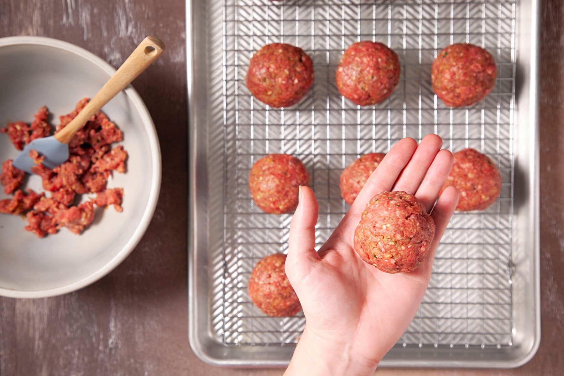 A person holding Beef mixture ball with other balls on baking tray