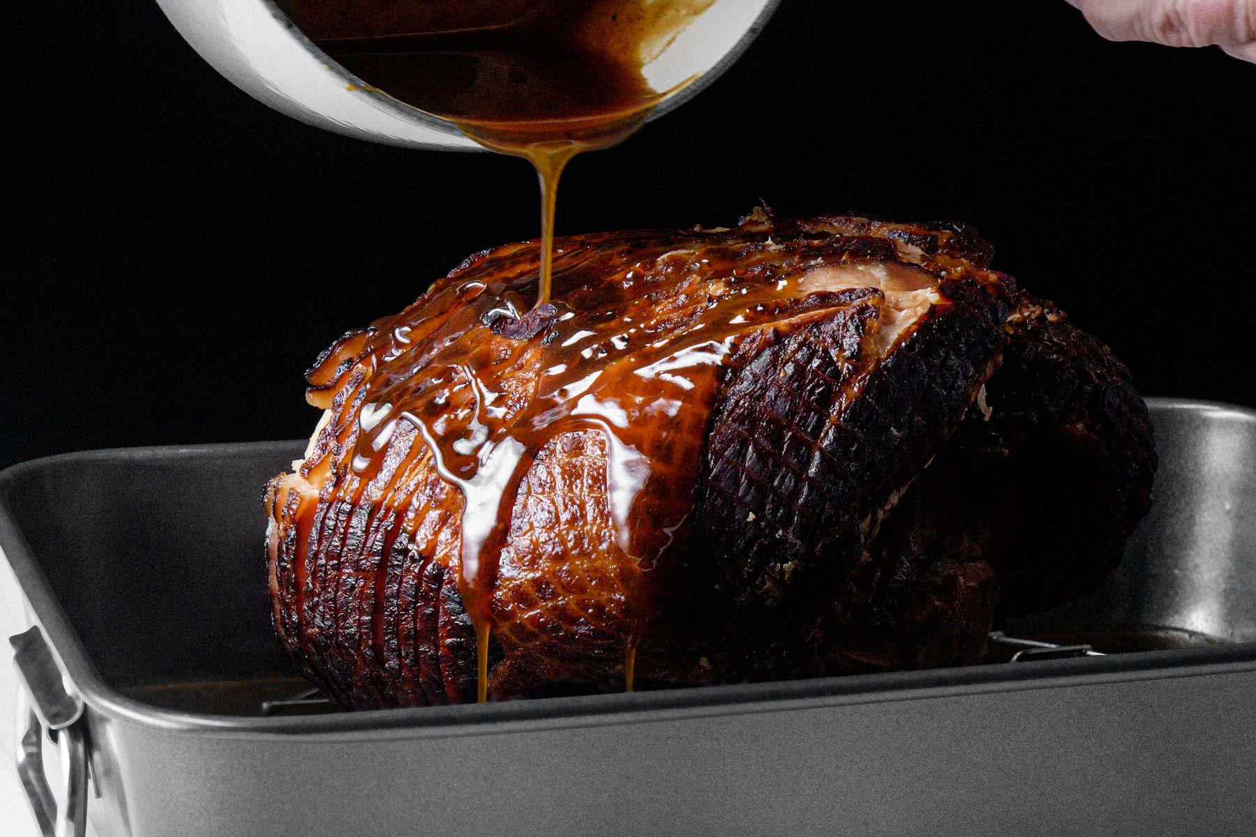 Pouring the Maple glaze over the ham on a baking tray