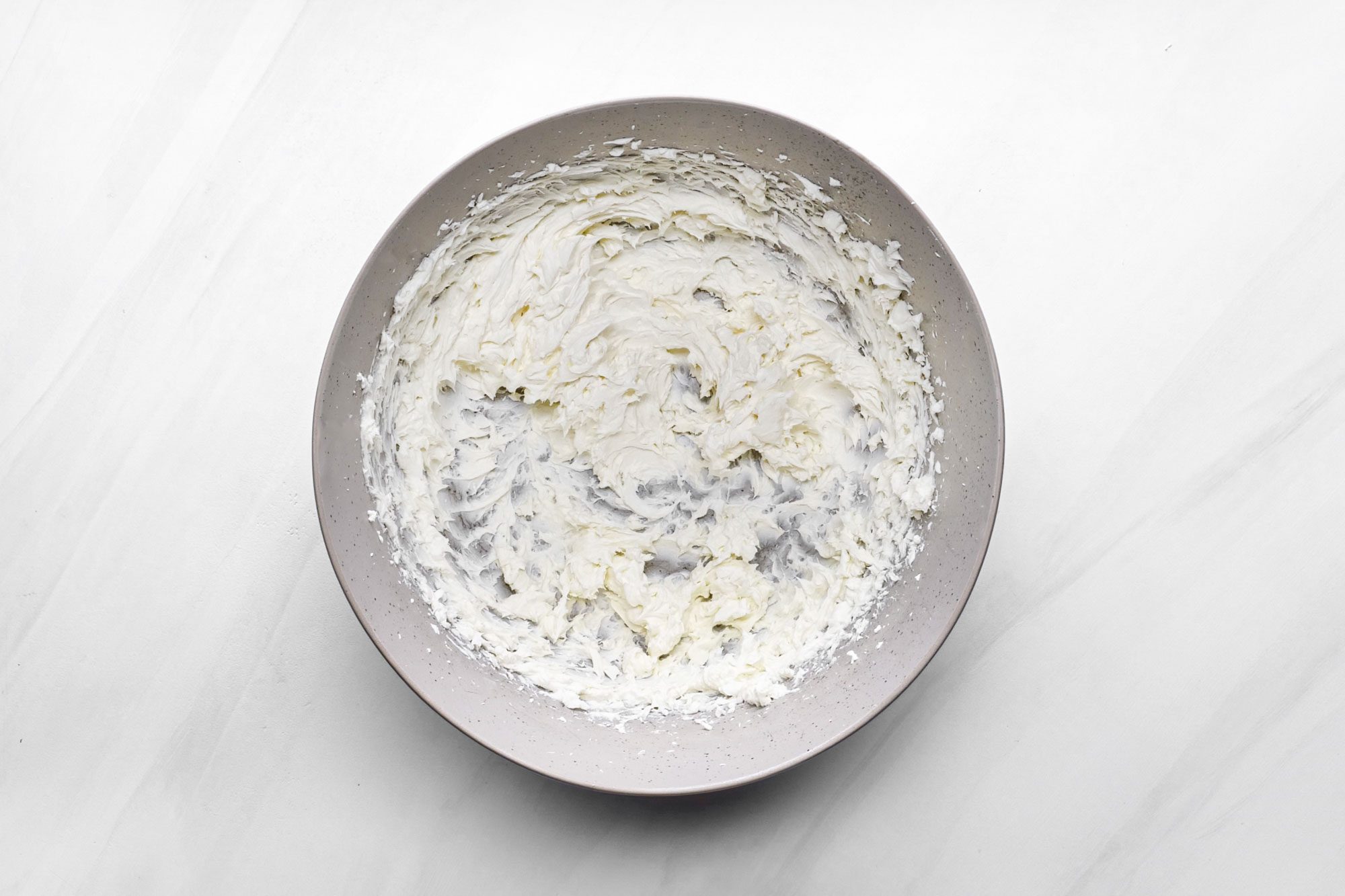 beaten cream cheese in a large bowl on marble surface