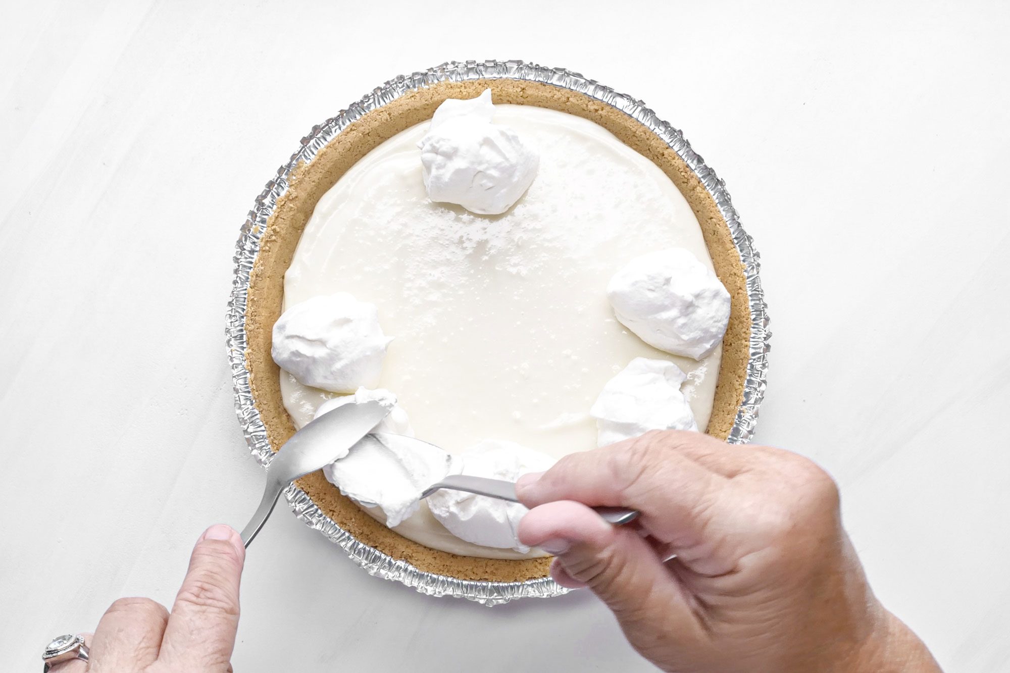 a person topping the pie with whipped cream on marble surface