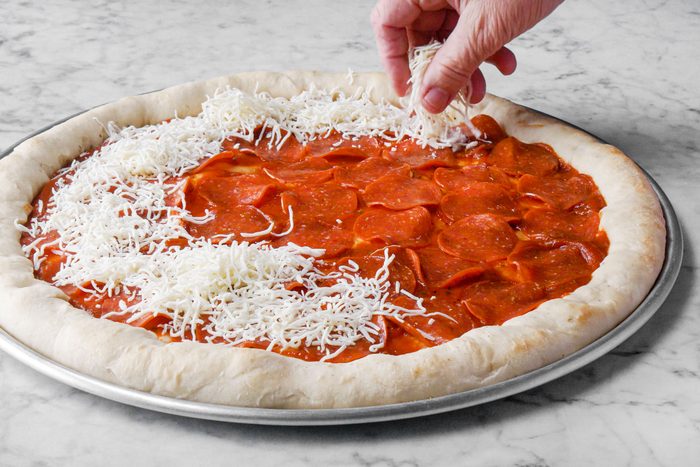 putting cheese on Pepperoni pizza