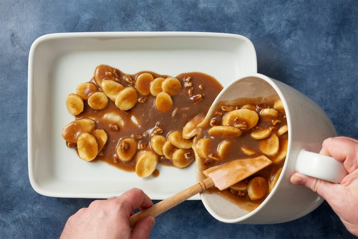 A person pouring banana foster mixture into a bowl of food