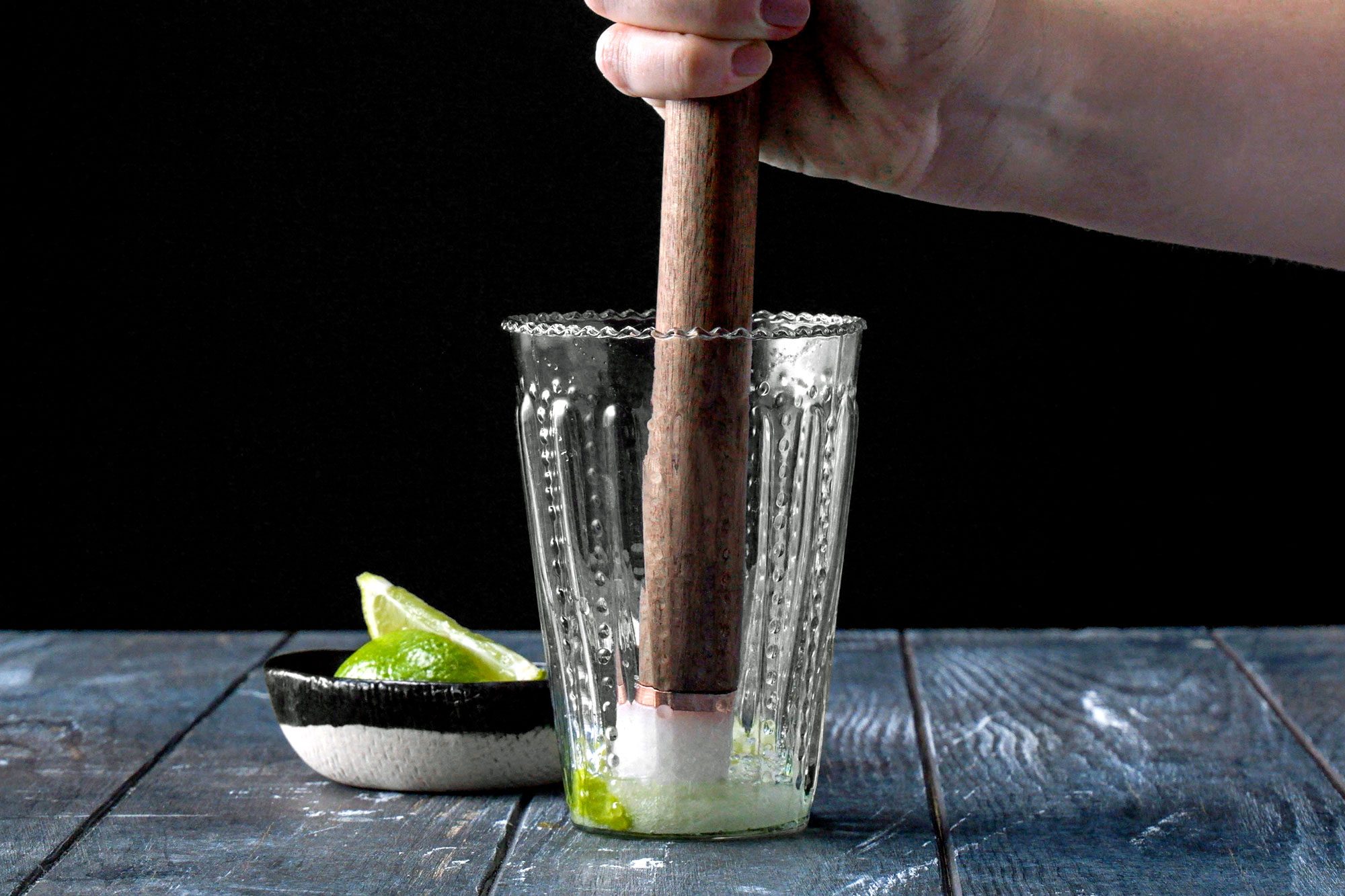 mashing mojito ingredients with a muddler in a highball glass