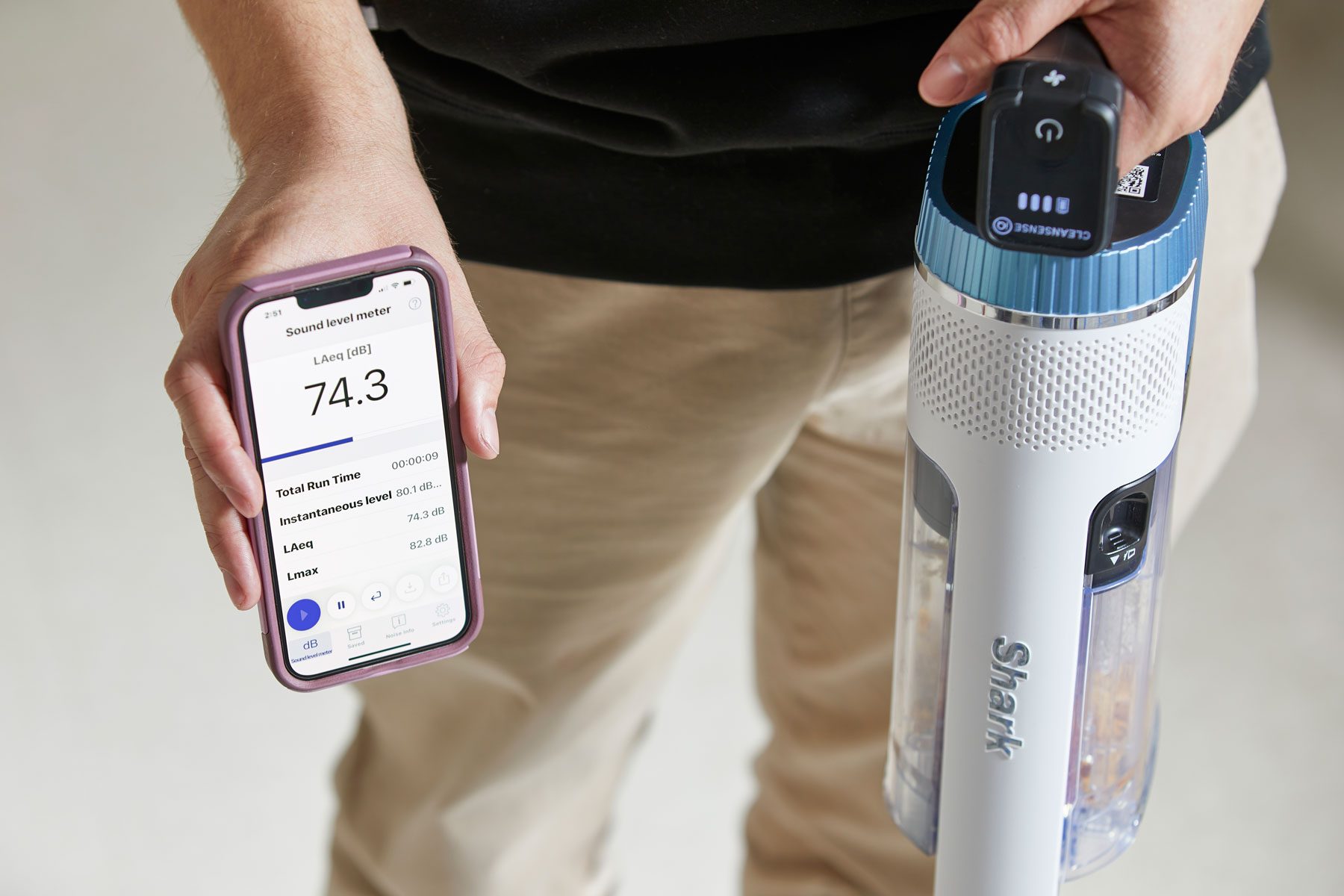 A man holding a phone showing Dyson app and hold a vacuum on the other hand