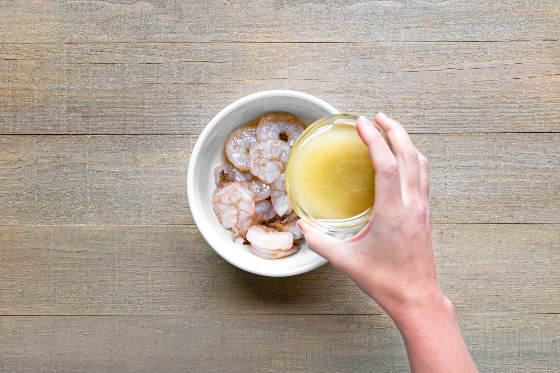 Pouring salad dressing on shrimps in a small bowl