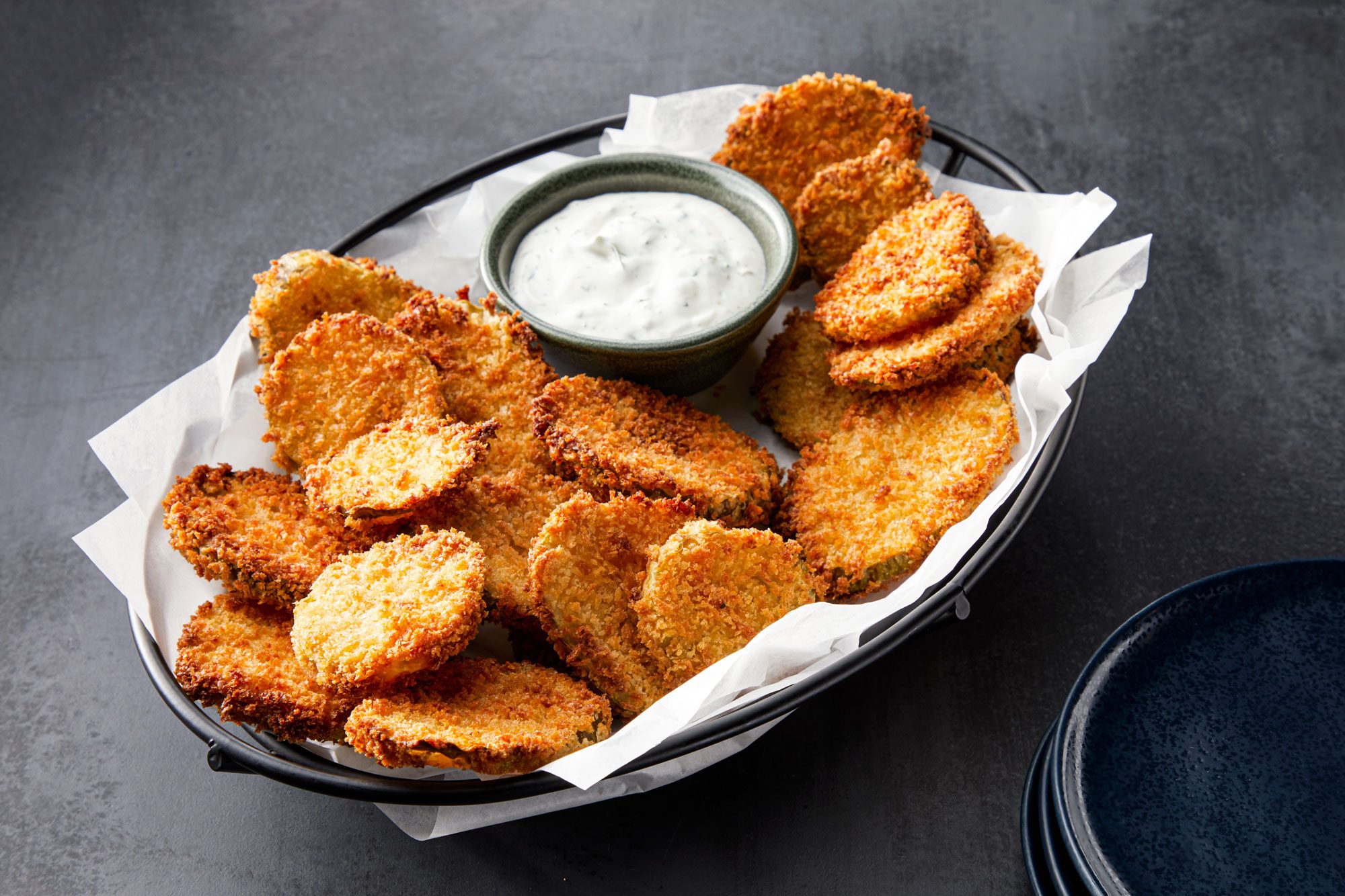 3/4 angle view shot of Air-Fryer Pickles served on tray with ranch; small plates; light black texture background;