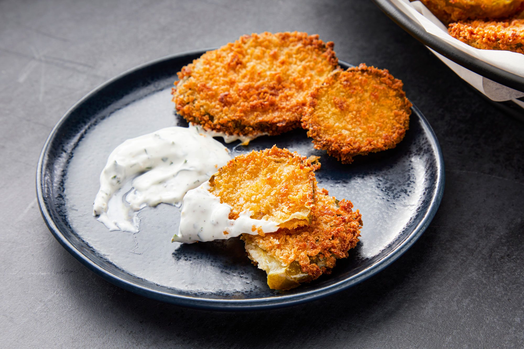 3/4 angle view shot of Air-Fryer Pickles served on small plate with ranch; light black texture background;