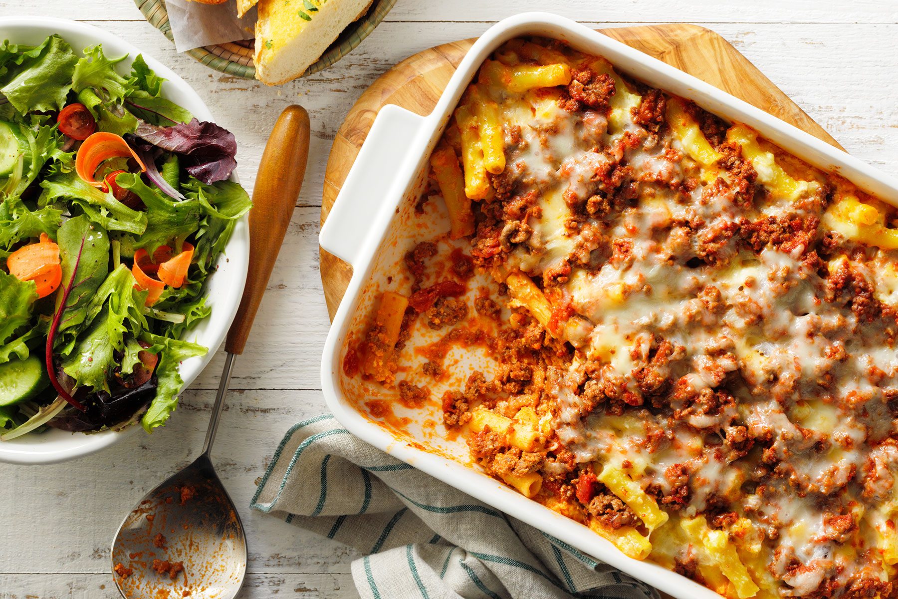 A casserole dish with pasta and meat and a salad