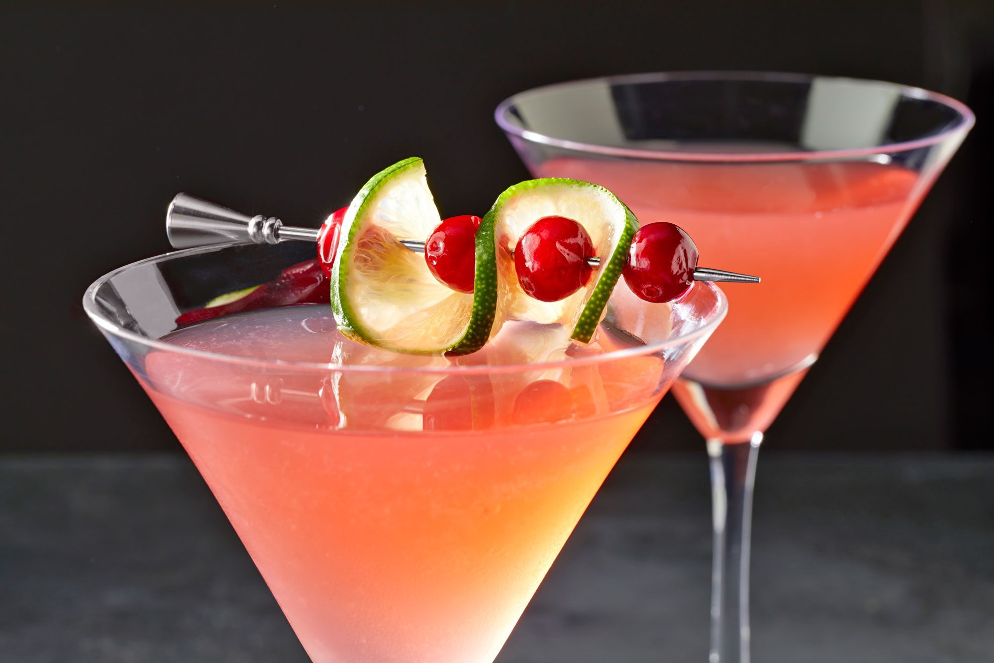 Two glasses of Cosmopolitan garnished with lime and cranberries
