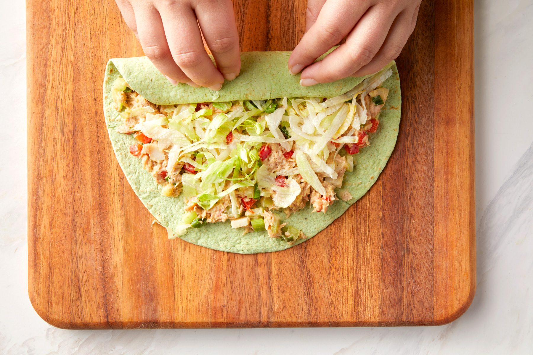 A person rolling the tuna salad tortillas