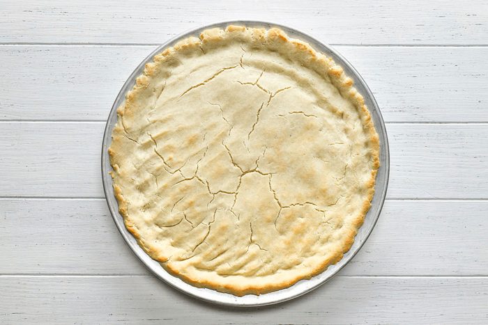 Gluten Free Pizza Crust on a pizza pan on white painted wooden surface