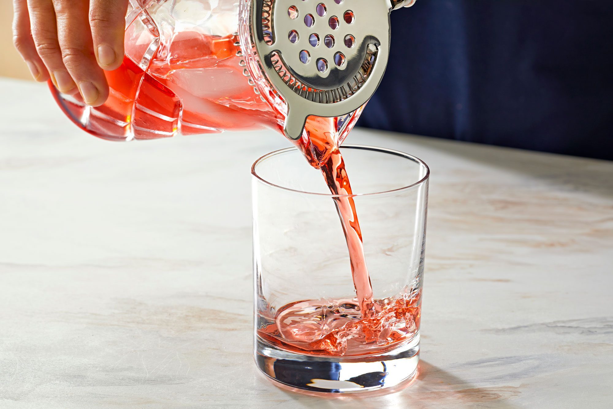 pouring negroni in a rock glass; marble surface;