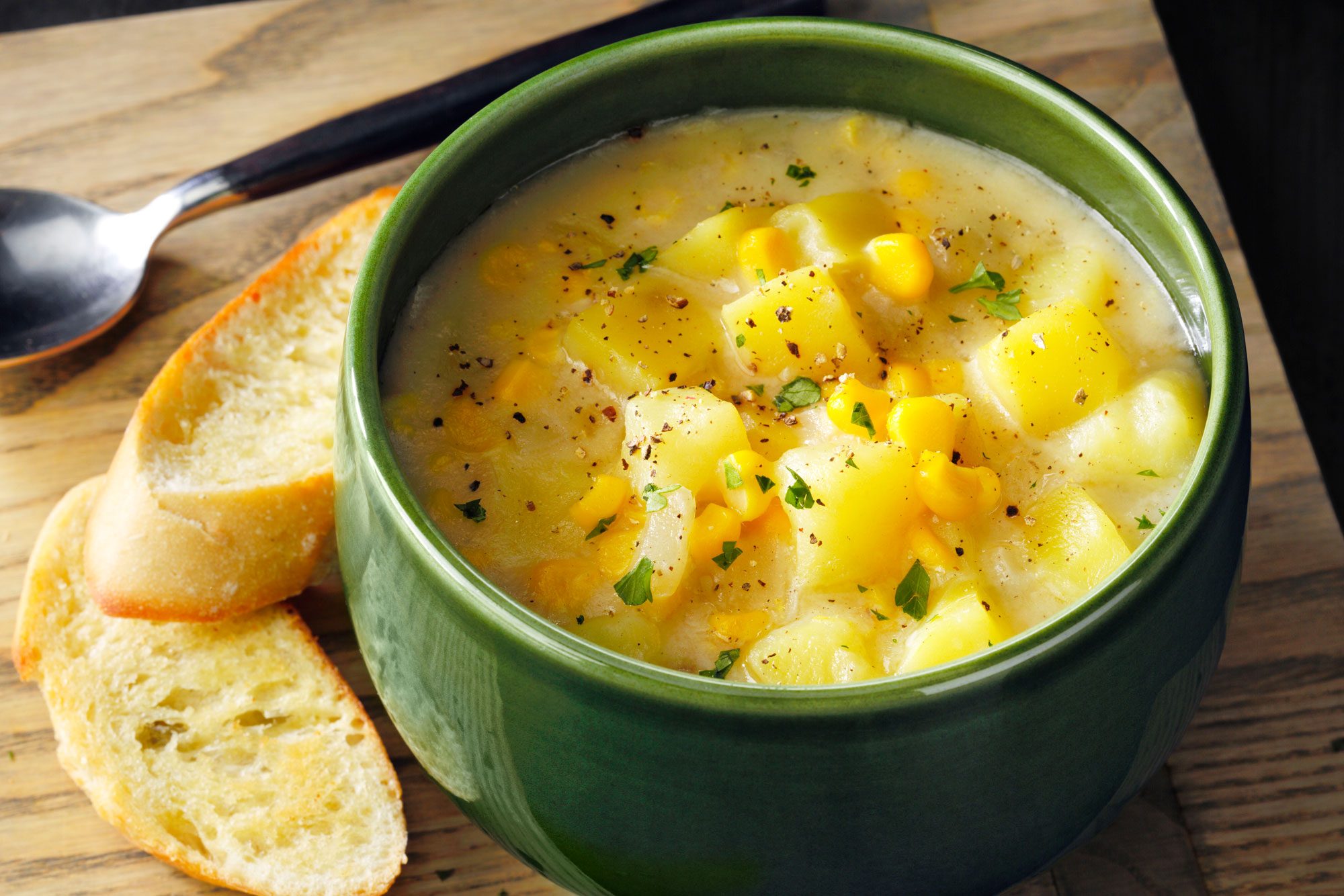 A bowl of Quick Potato Corn Chowder soup with bread on a wooden cutting board
