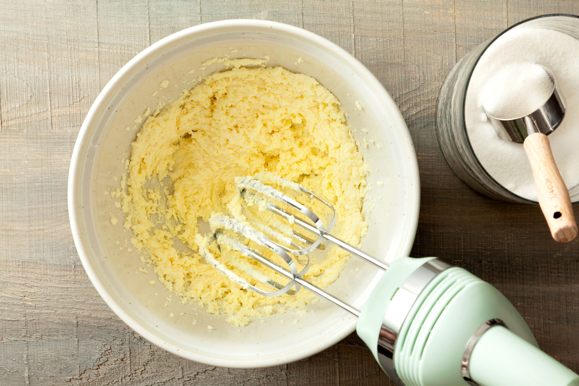 in a large bowl mixing butter and sugar using hand mixer on a wooden surface