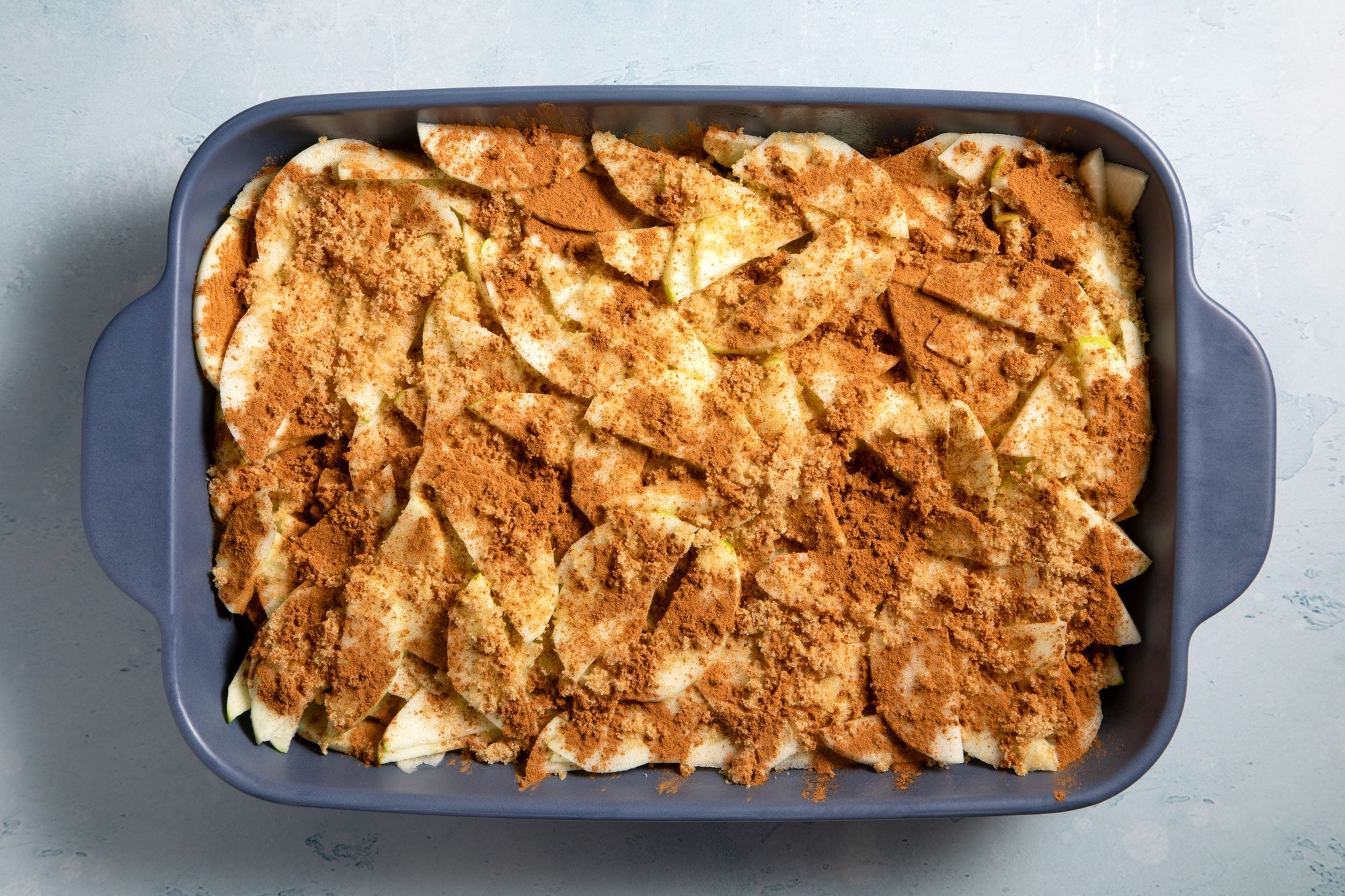 overhead shot; light blue textured background; apples in a greased baking dish, Sprinkled with brown sugar and cinnamon;