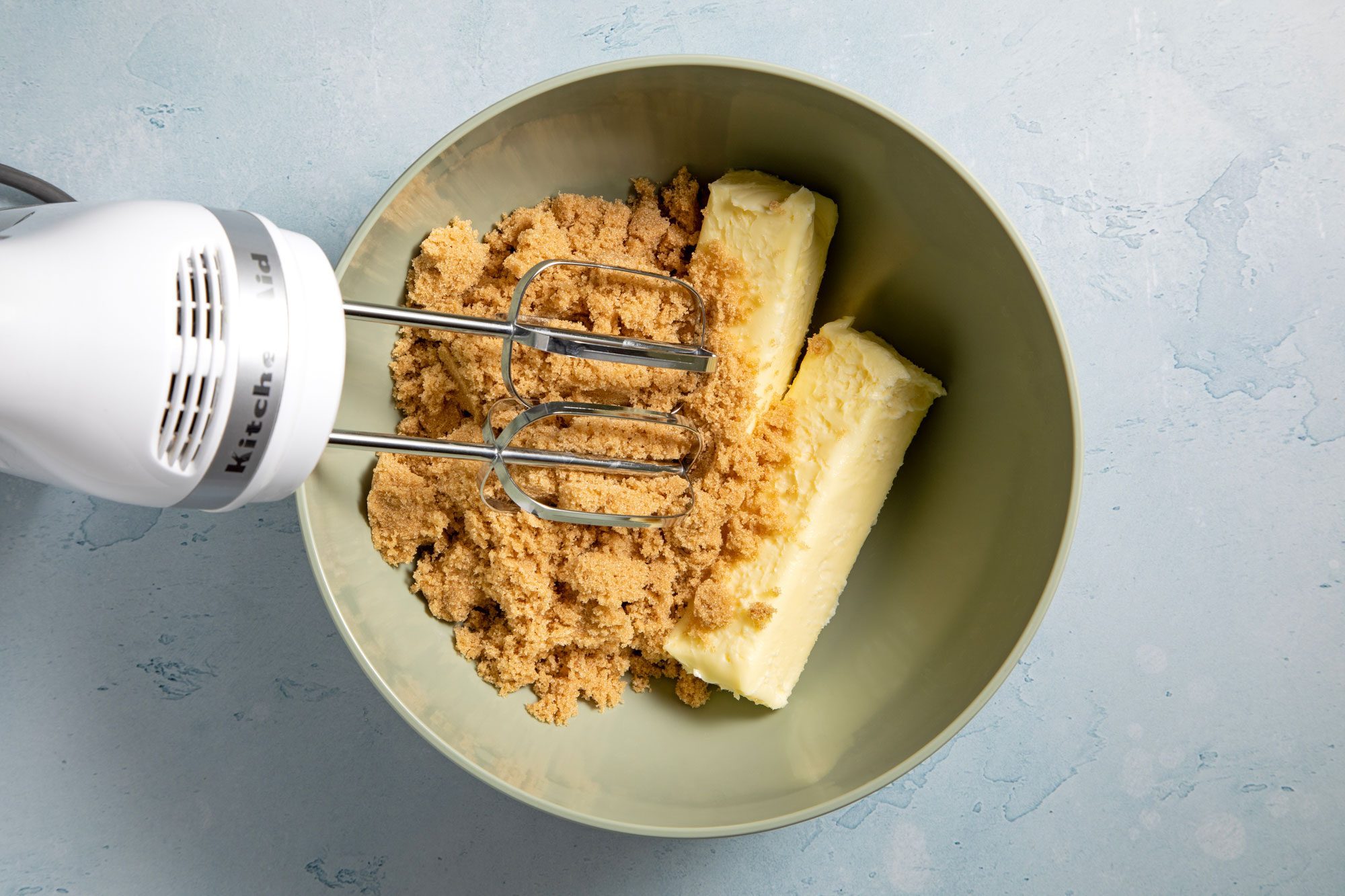 overhead shot; light blue textured background; In a bowl, beating cream butter and remaining brown sugar;