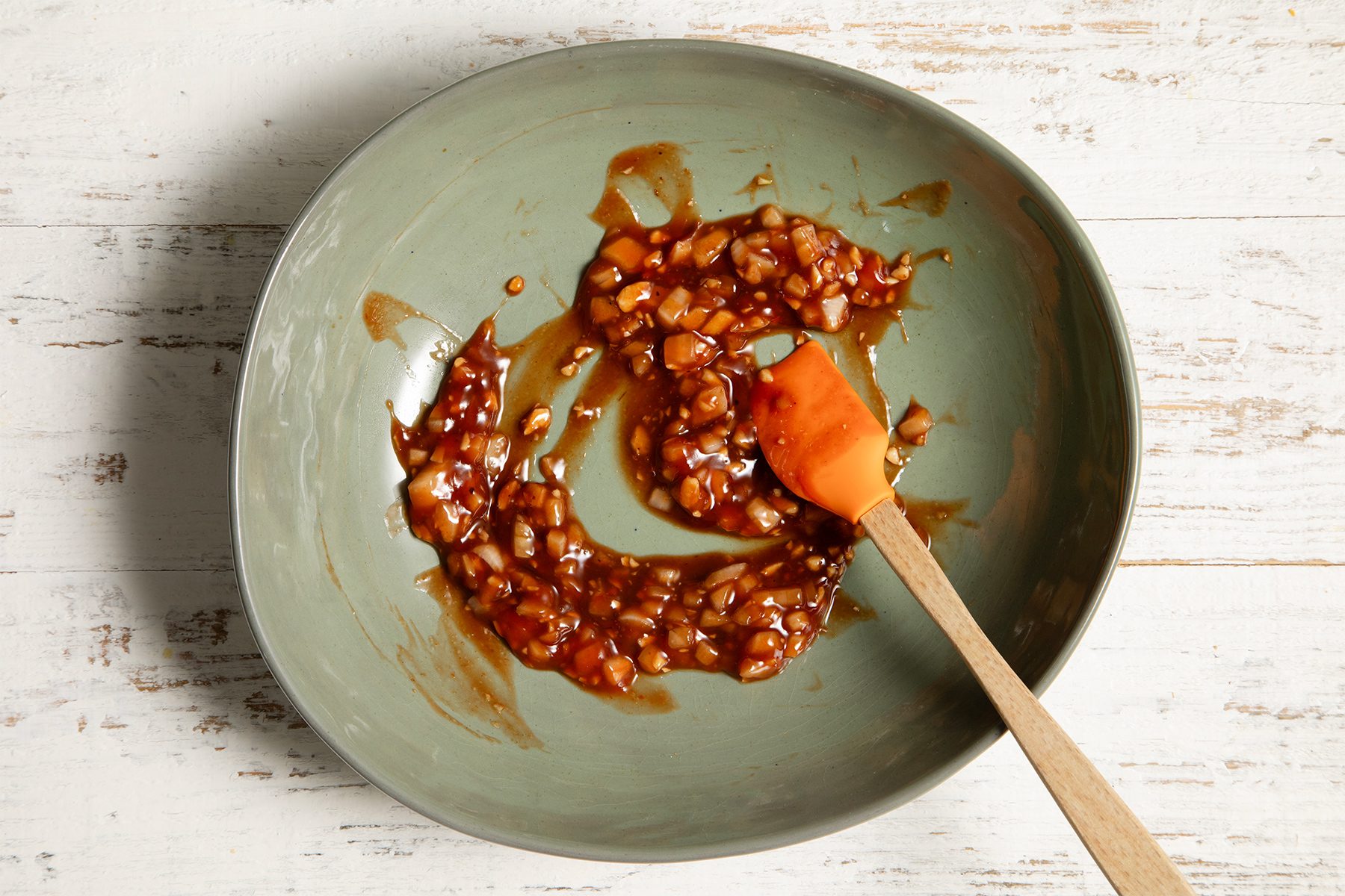A light green mixing bowl containing a mixture of chopped onions in a brown sauce.