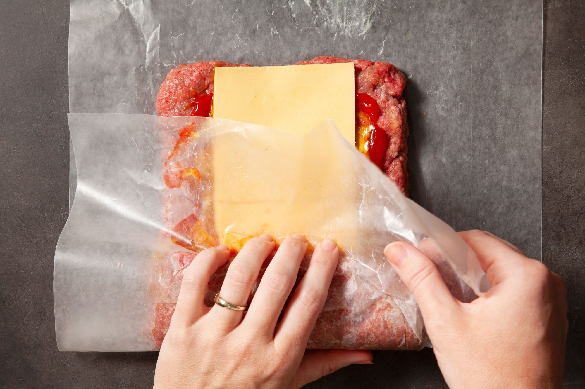 Overhead shot of roll up loaf like jelly-roll style; starting with a short side; and pulling away waxed paper while rolling; black texture background;
