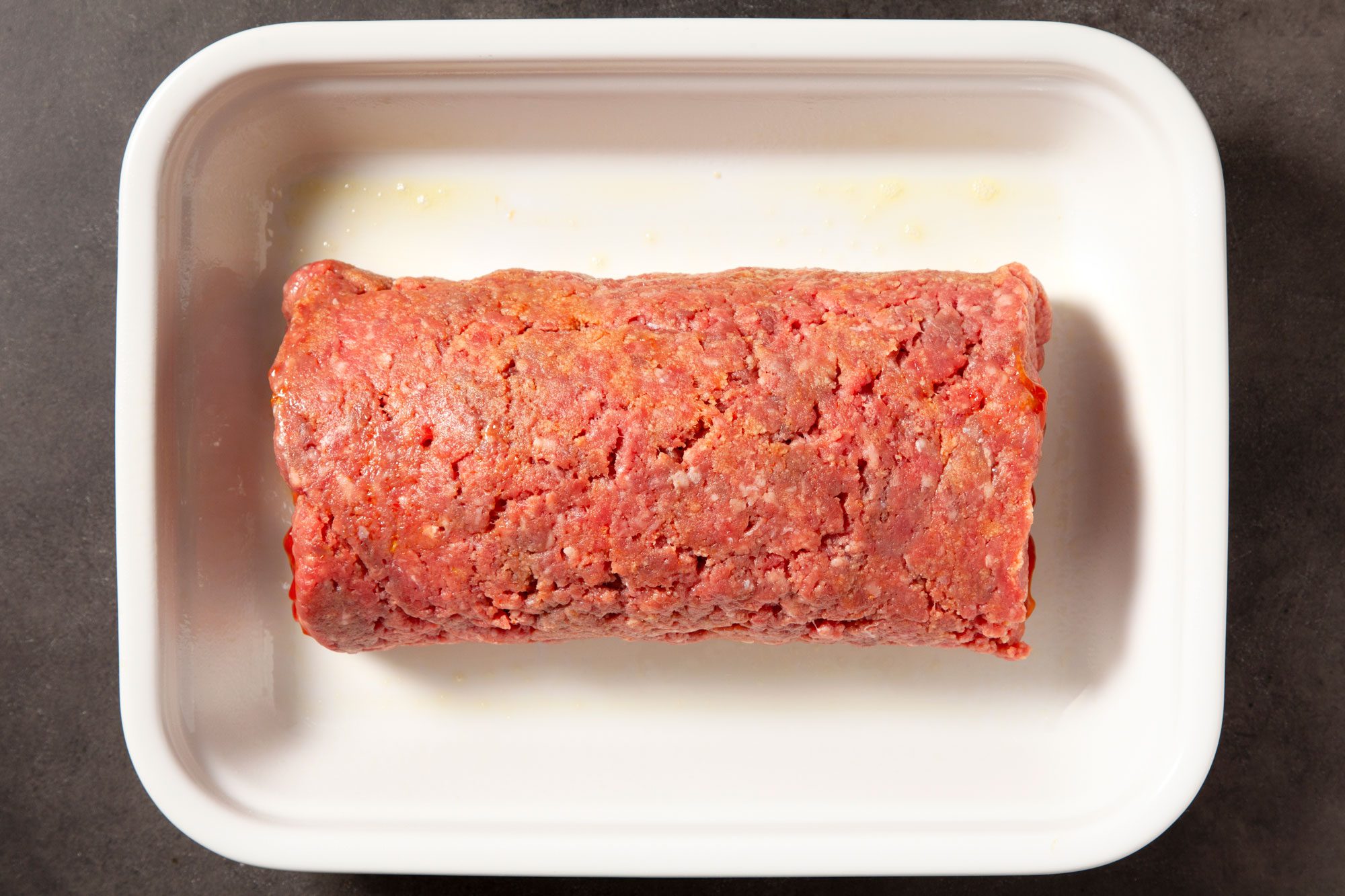 Overhead shot of meat loaf; seam side down in a greased baking pan; black texture background;