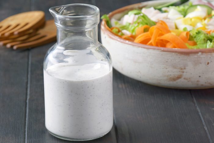 A glass container of Homemade Ranch Dressing with a bowl of salad