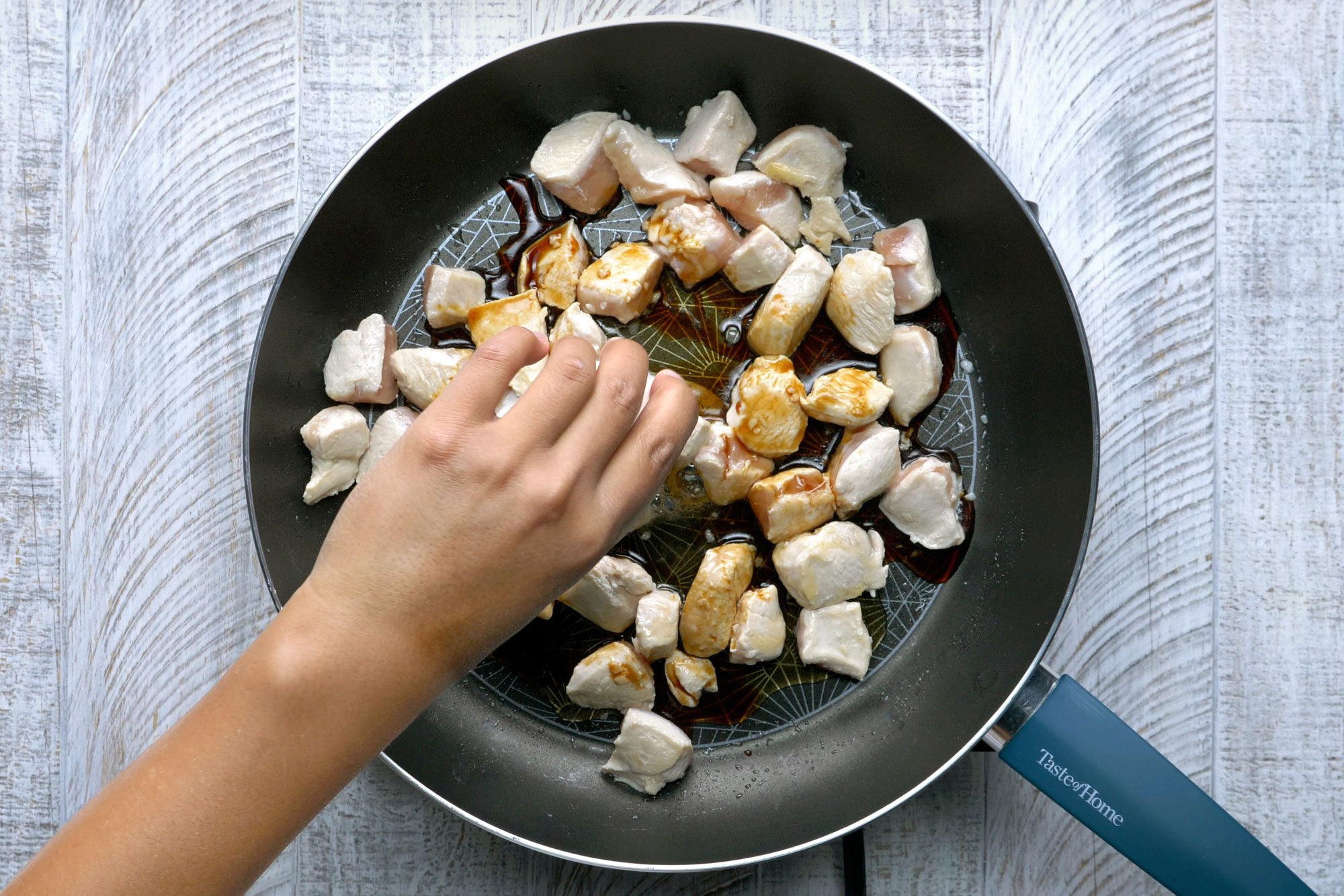 Overhead shot of a large nonstick skillet; heat two teaspoons oil over medium-high heat; stir-fry chicken and garlic 1 minture; add honey; soy sauce; salt and pepper; cook and stir until chicken is no longer pink; wooden background;