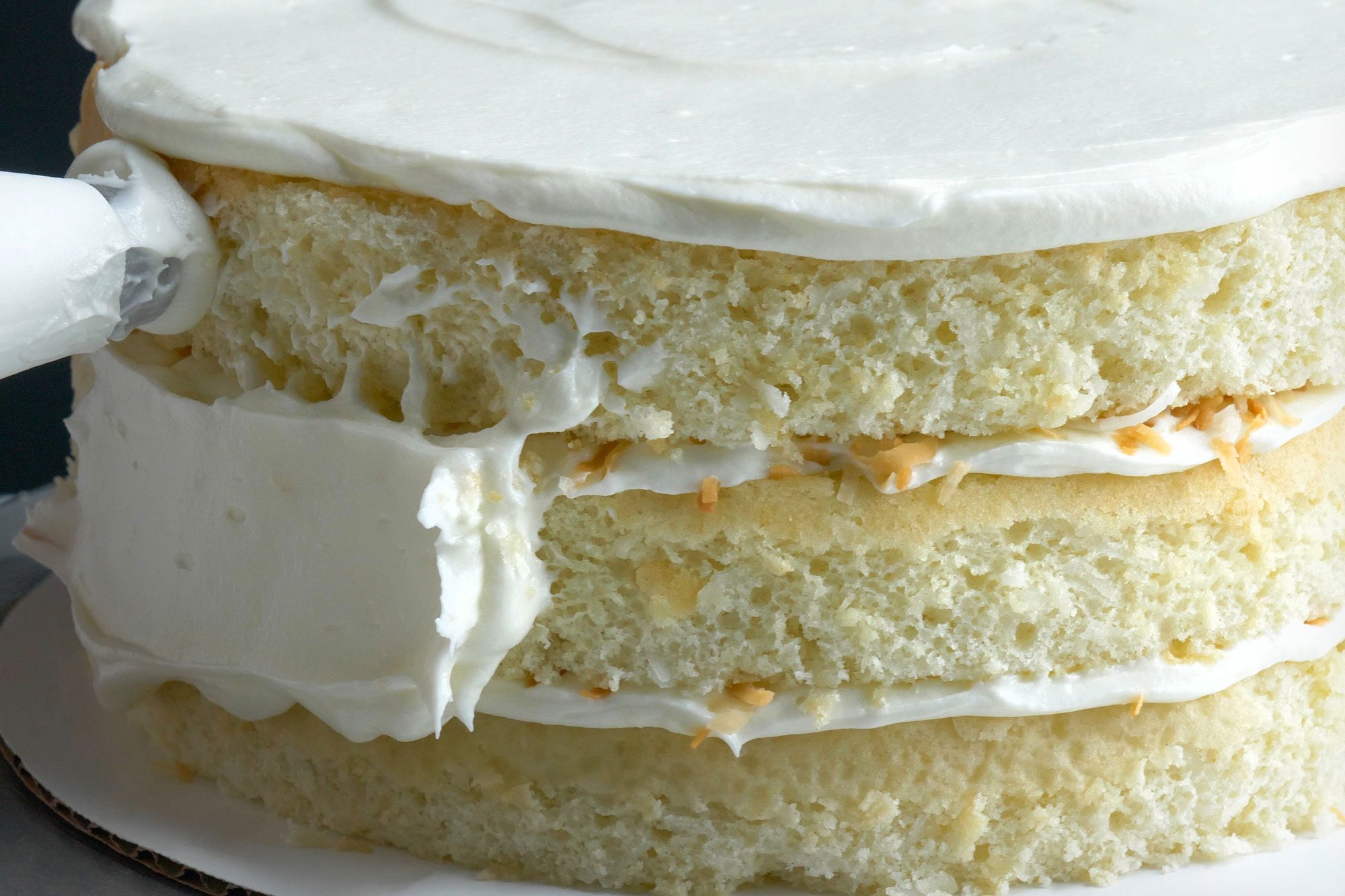 Close shot of spreading frosting over top and side of cake;
