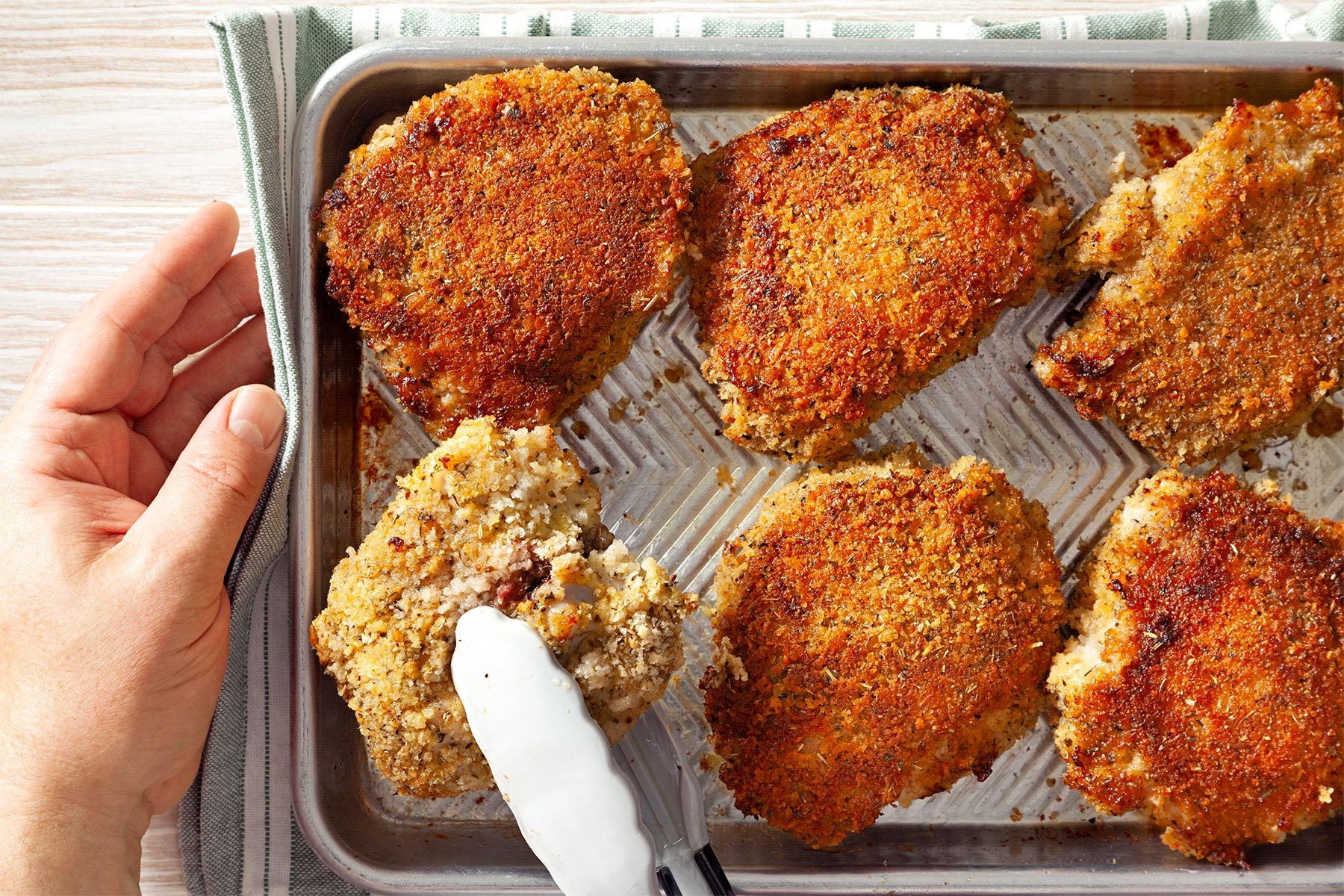 flipping baked chicken with tong in baking tray