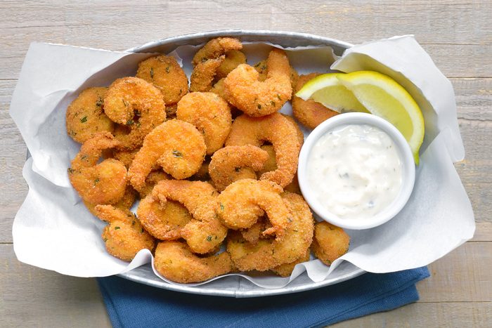 Overhead shot of Popcorn Shrimp; served on large platter; with sauce and lime wedges; blue napkin; wooden background;